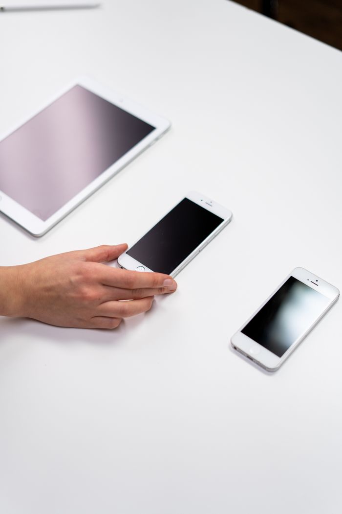 Vue de dessus d’une installation minimaliste présentant une tablette et des smartphones sur une surface blanche.